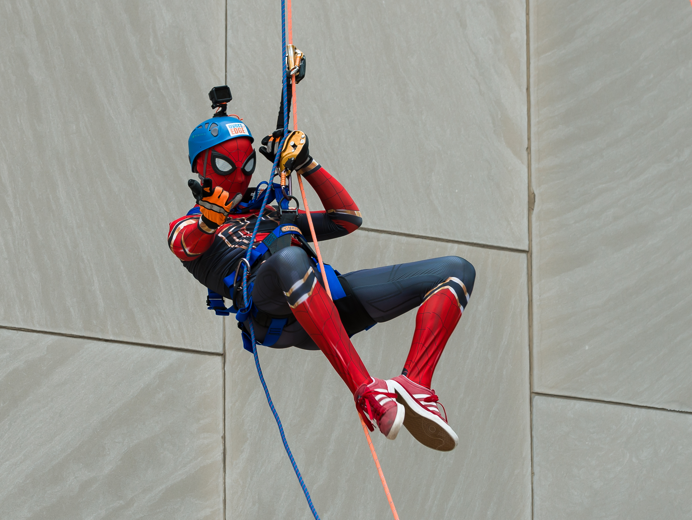 Person dressed as Spider-Man rappelling down a building, wearing a helmet.