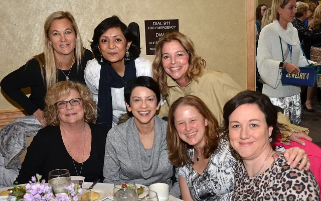 Group of seven women smiling at a dining table with food and drinks.