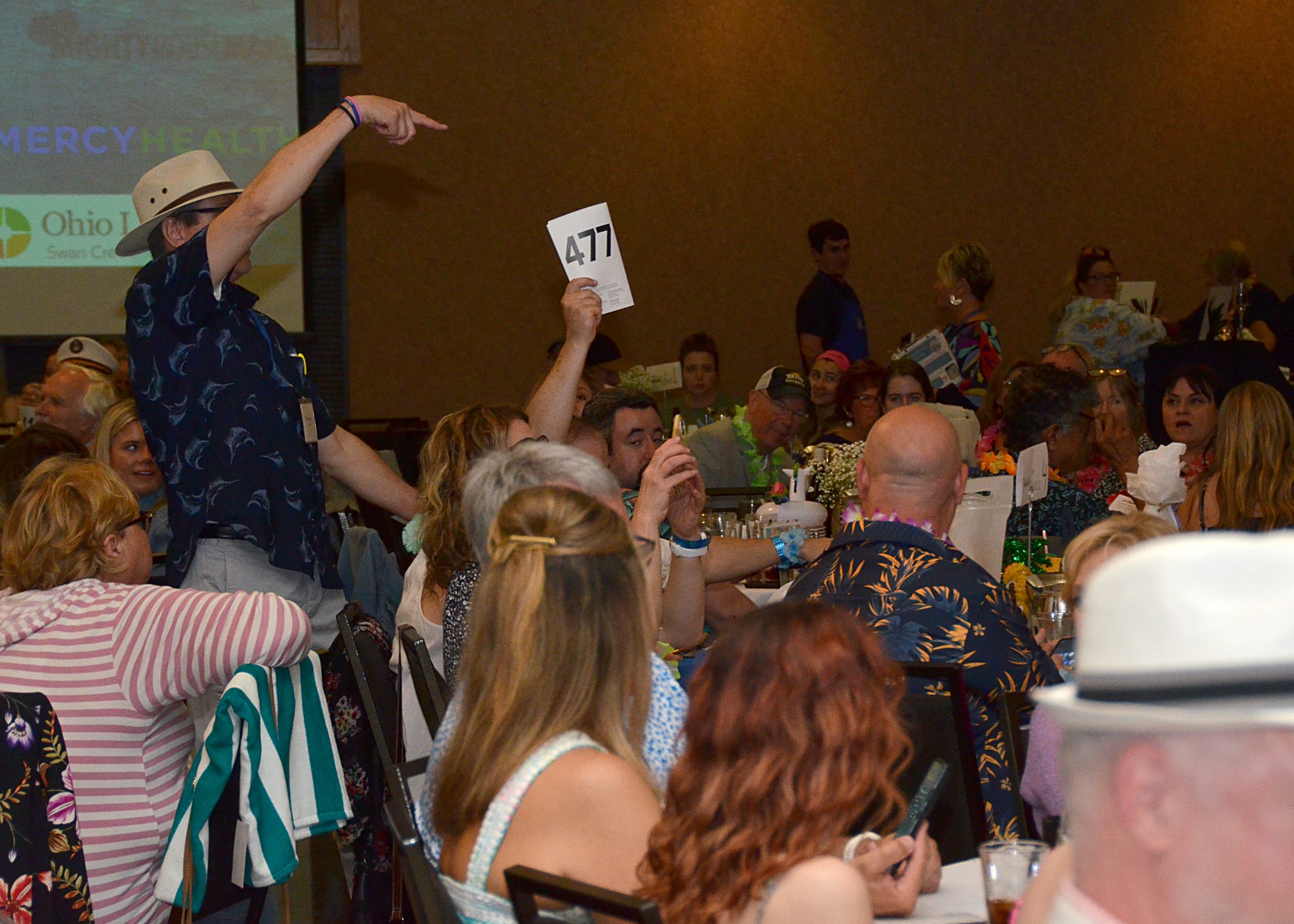 Crowd at an indoor event, one person raising a card.