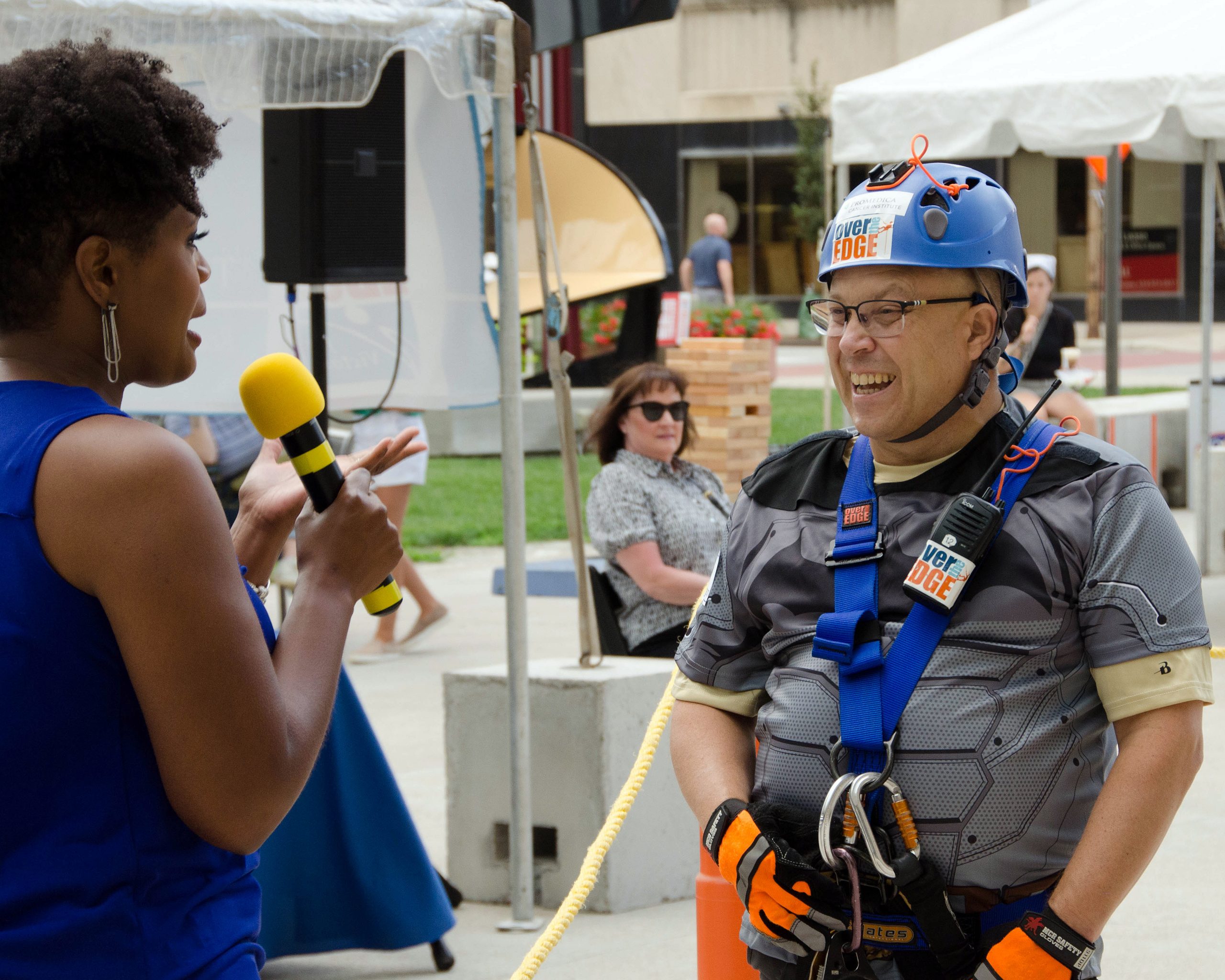 Woman with microphone interviews man in climbing gear.
