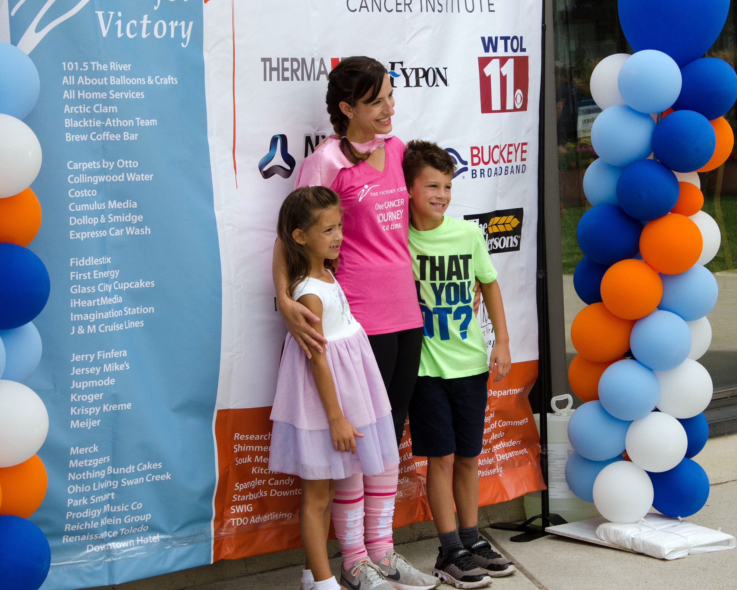 Woman and two children pose at an event, surrounded by colorful balloons.