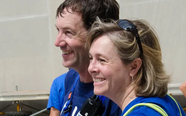 Man and woman smiling on a boat deck, wearing blue shirts.