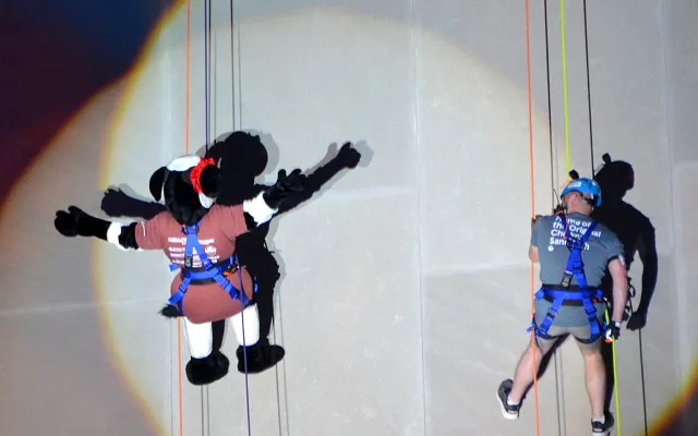 Two people in harnesses rappelling down a wall, one in costume.
