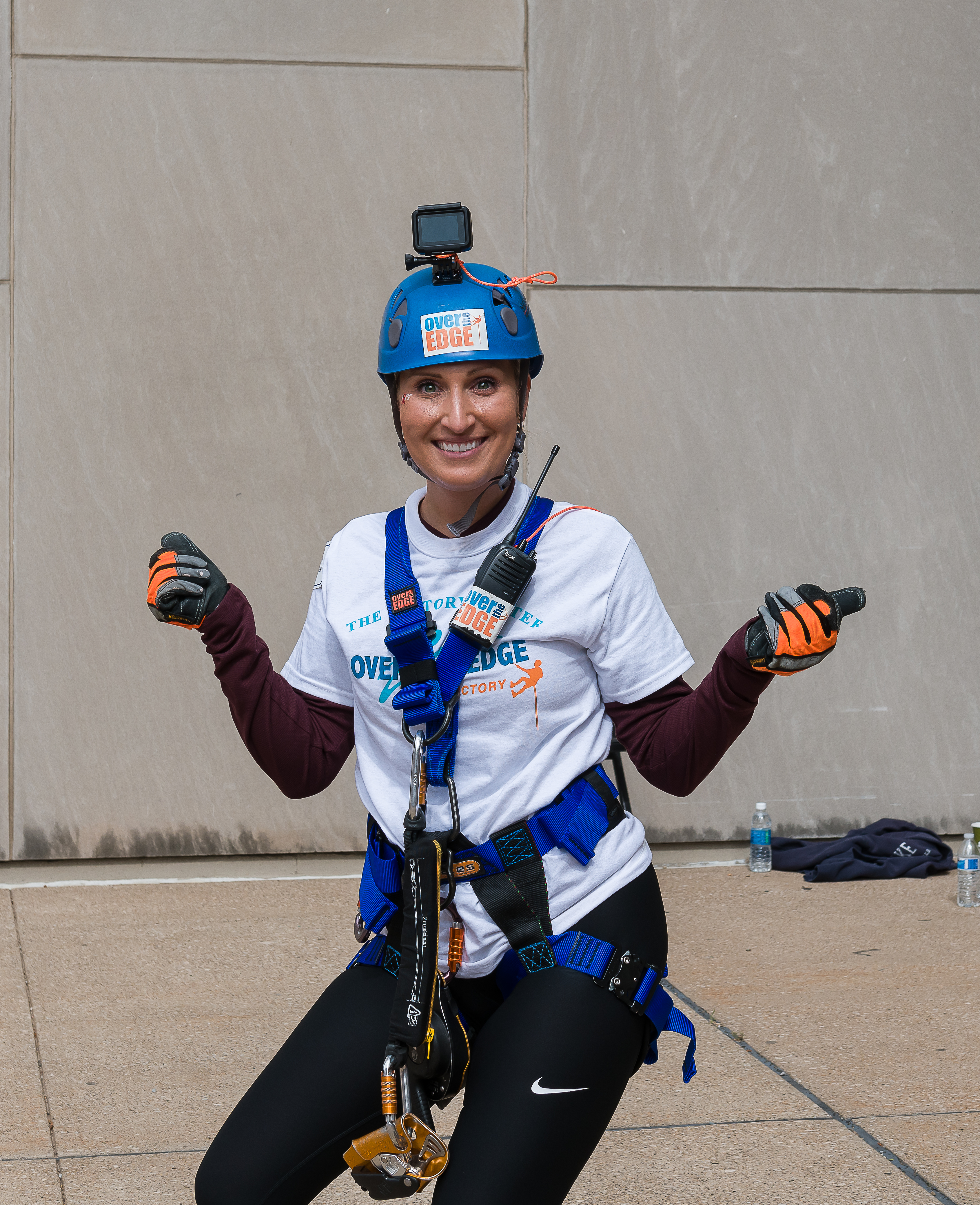 Person in climbing gear and helmet smiling at camera, urban setting.
