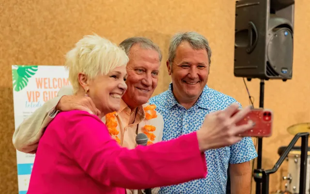 Three people smiling and taking a selfie at an indoor event.