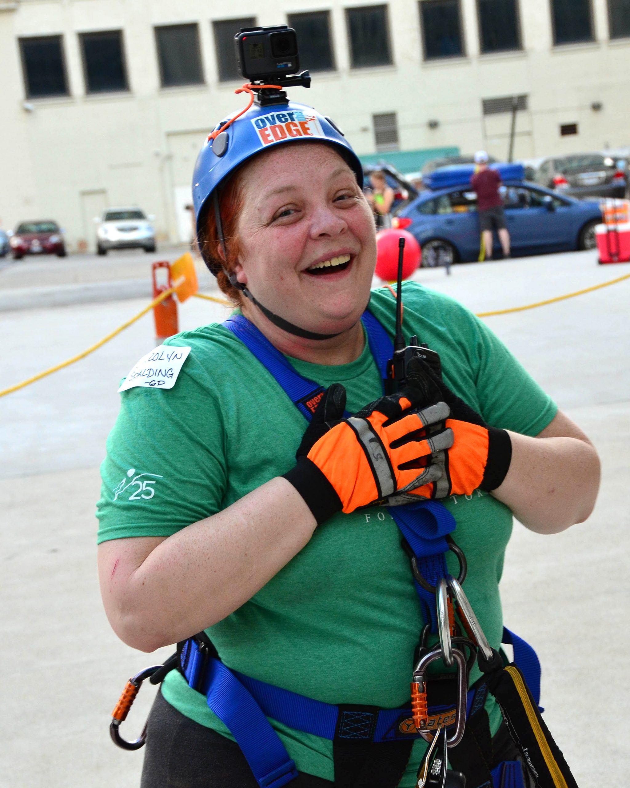 Woman in a helmet and harness, smiling outdoors.