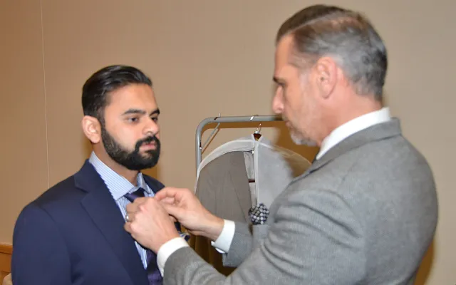 Man adjusts another man's tie in a formal setting.
