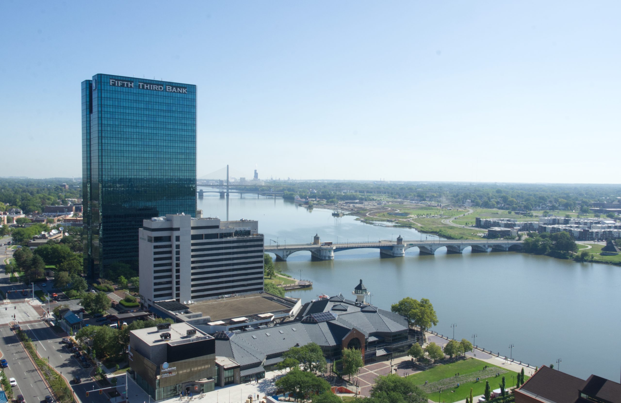 Cityscape with tall glass building, river, and bridge on a clear day.