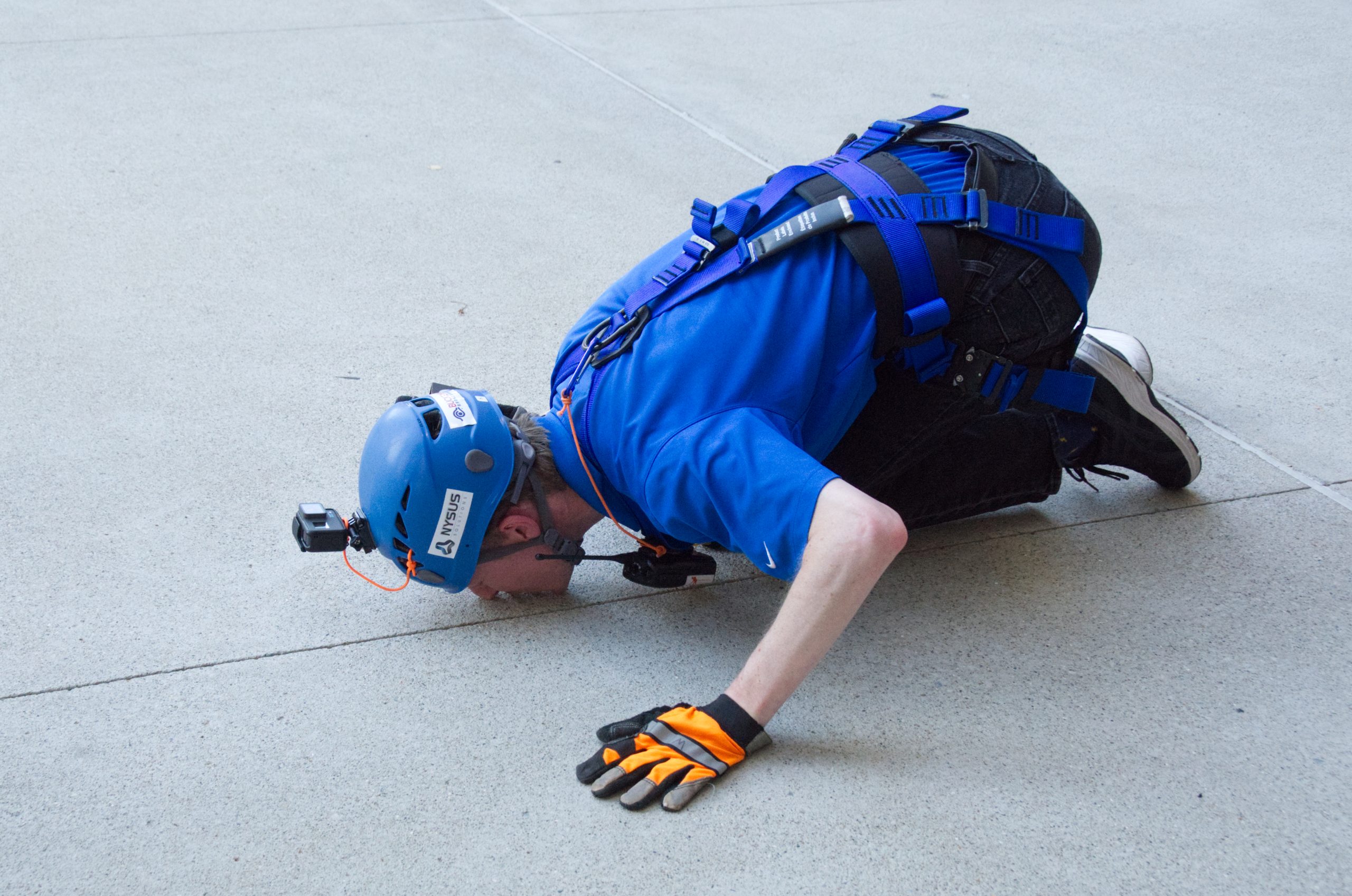 Person in blue gear kneeling on concrete, wearing a helmet and gloves.