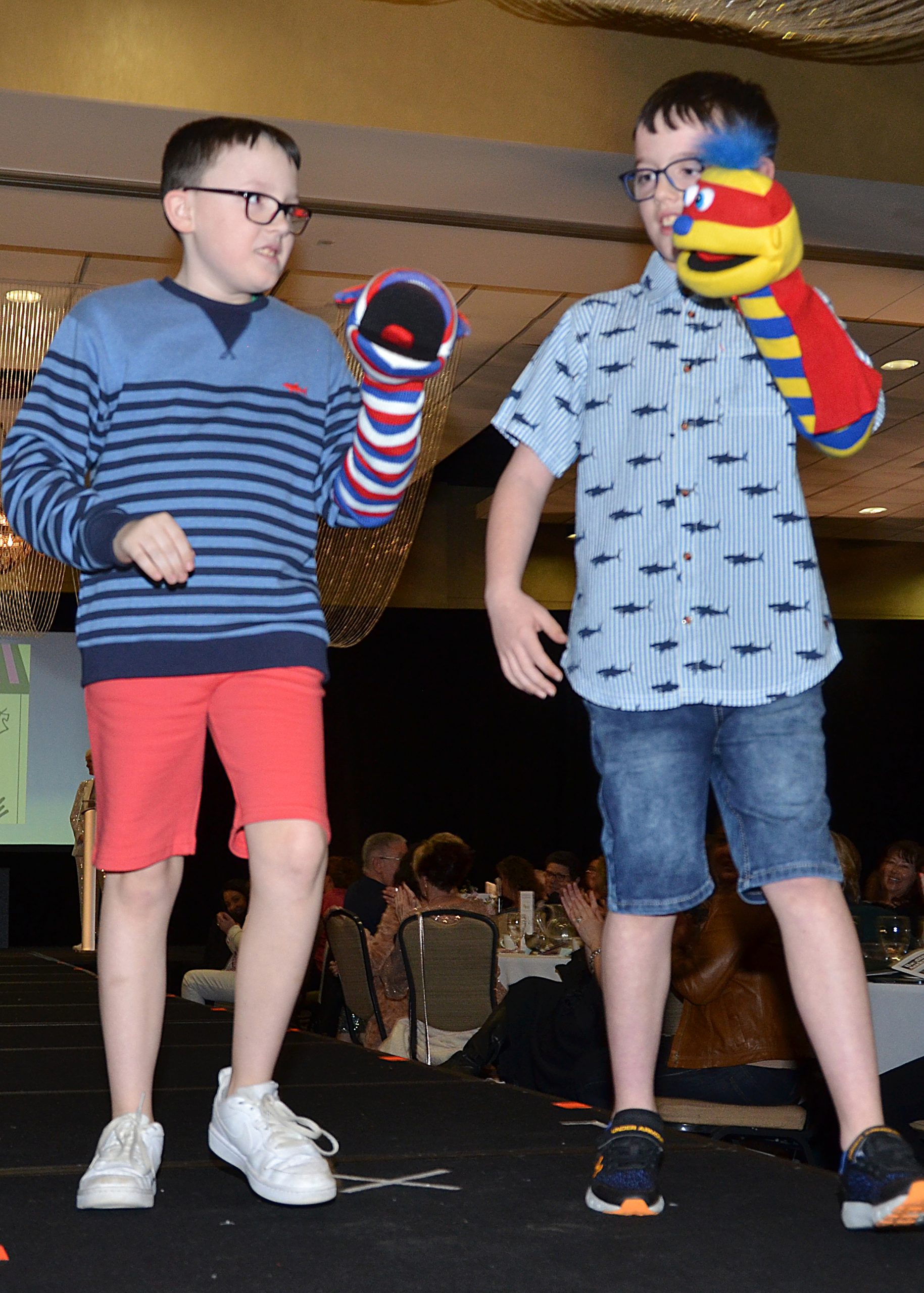 Two children with sock puppets perform on stage.