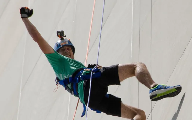 Man in helmet and harness joyfully rappels down a tall wall.