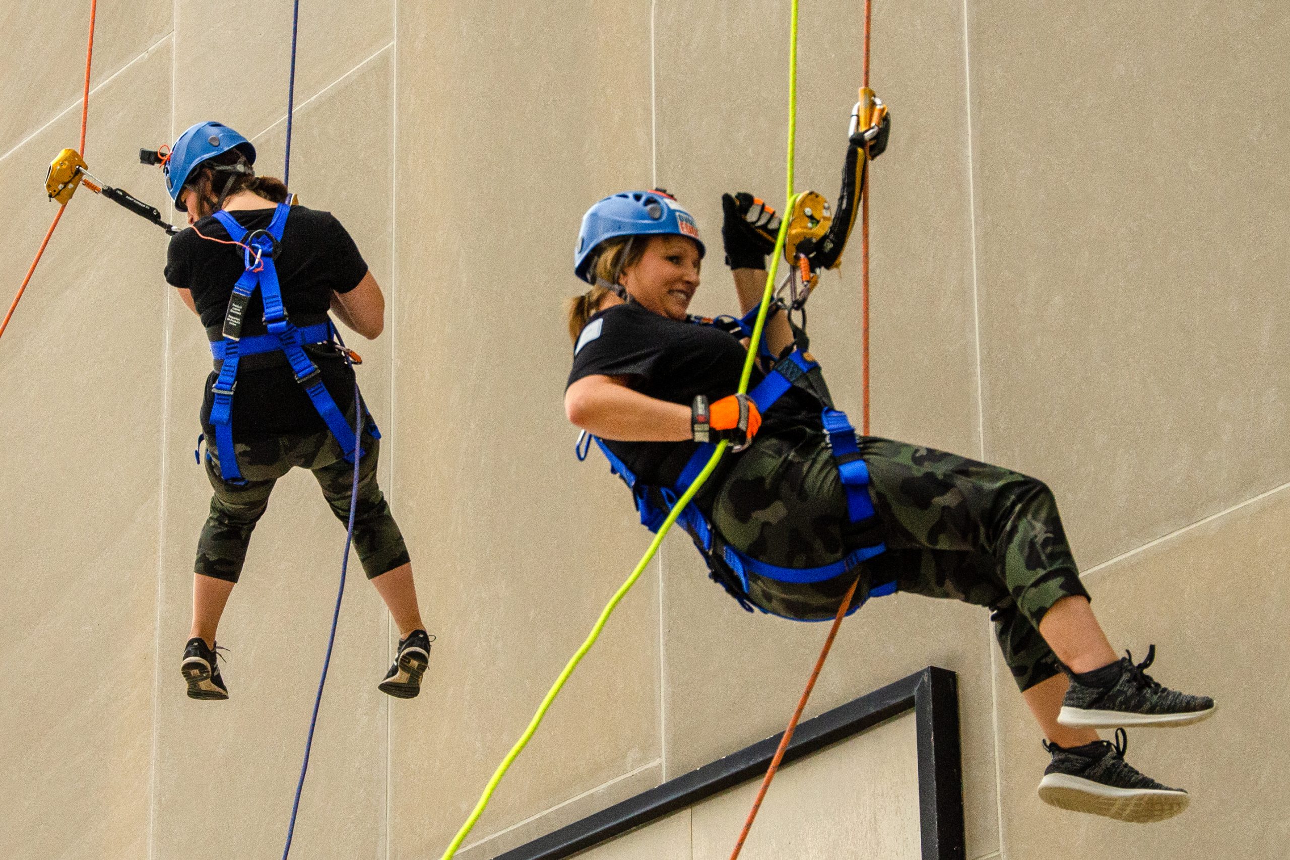 Two people in helmets rappelling down a building.