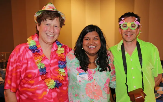 Three people in colorful tropical shirts smiling at an event.
