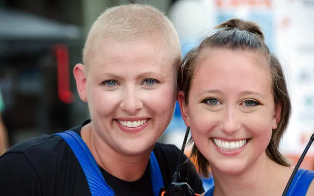 Two people smiling in blue outfits, outdoors, close together.