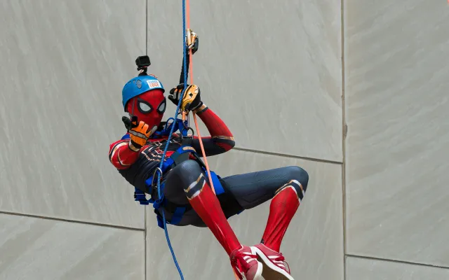 Person dressed as Spider-Man rappelling down a building, wearing a helmet.