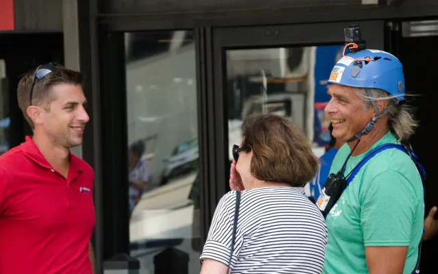 Three people chatting outdoors; one man wears a helmet and harness.