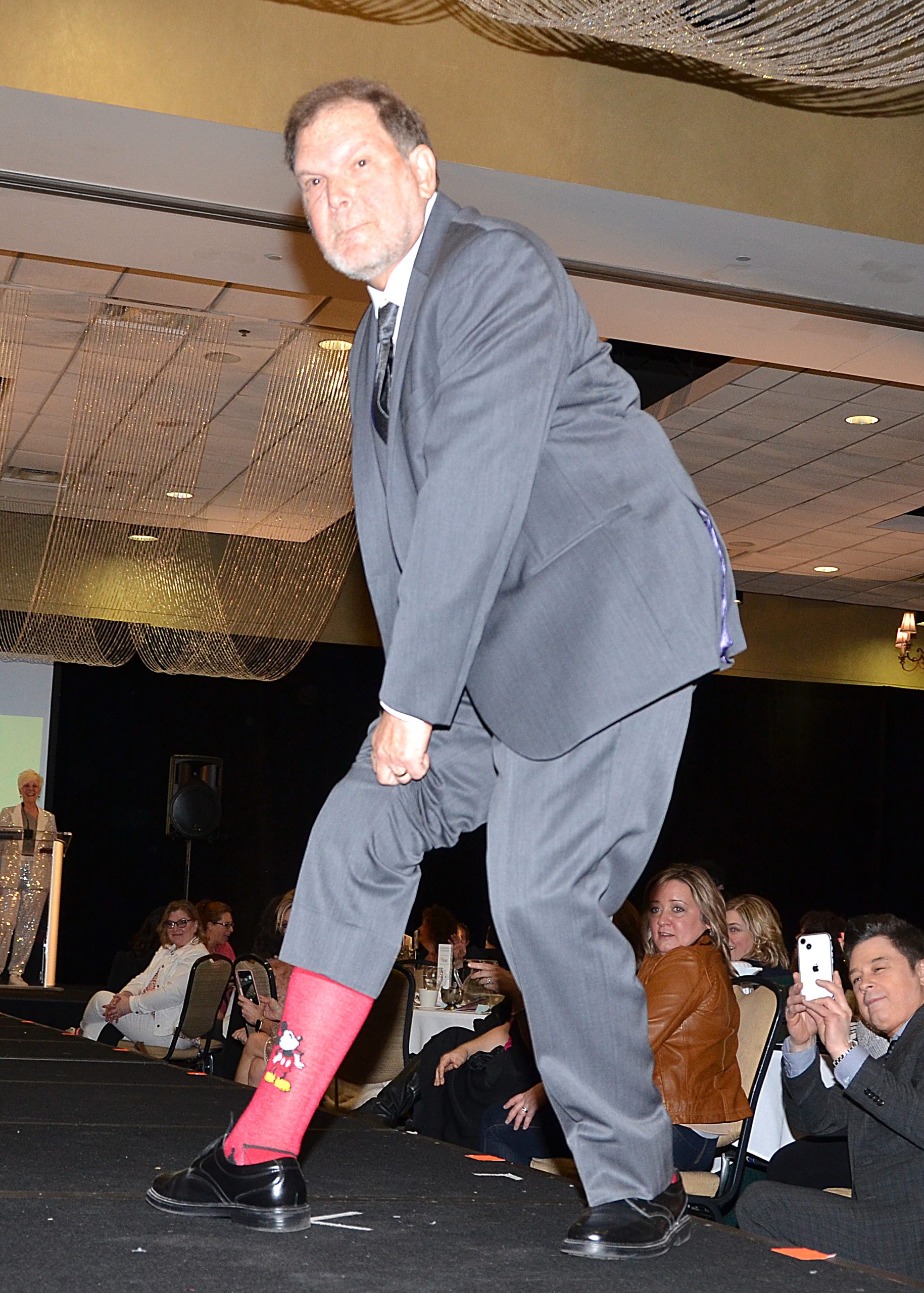 Man on stage showing off red socks to audience.