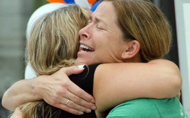 Two women embrace tightly, one looking emotional.