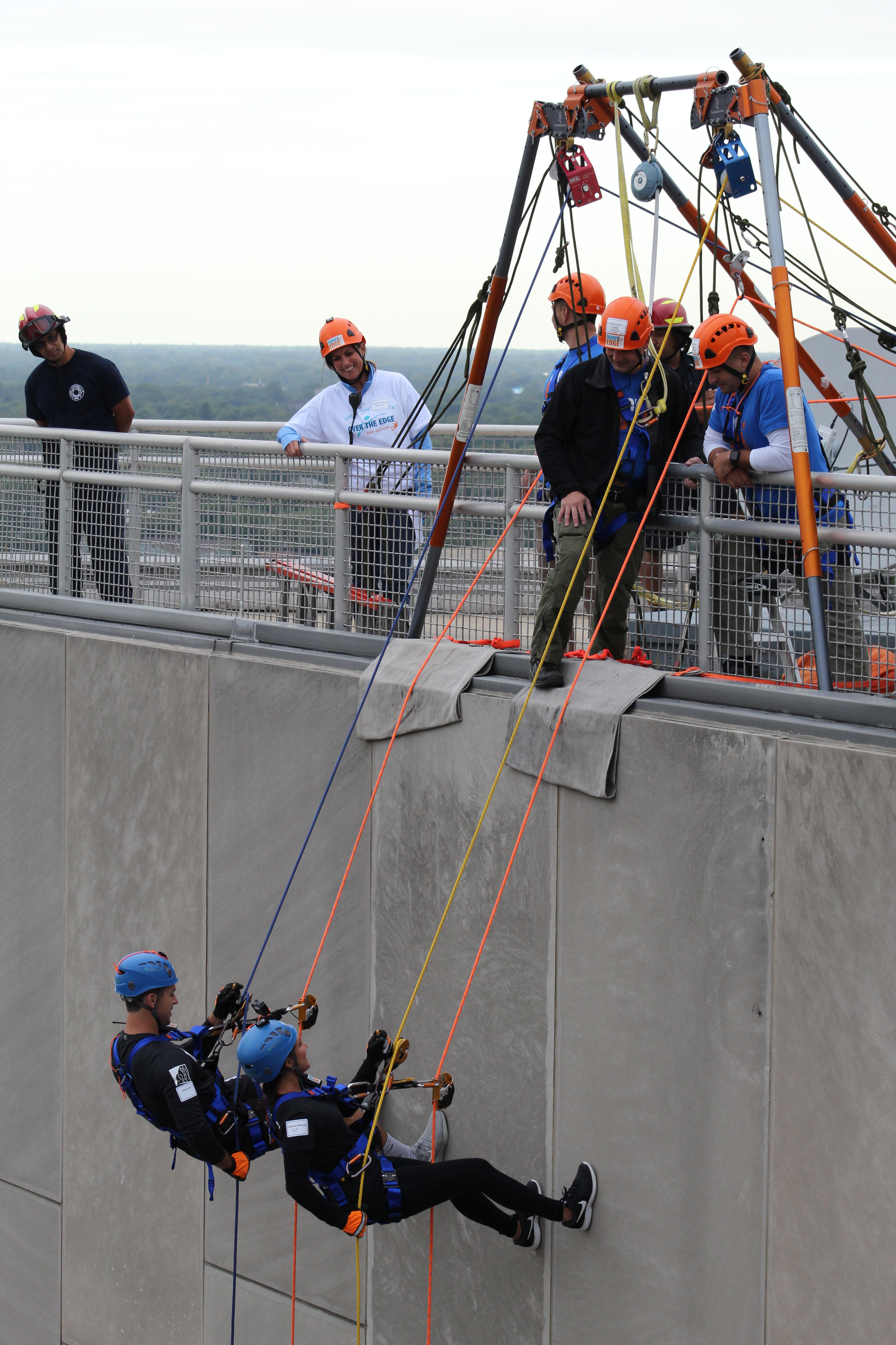 People rappelling down a building as others watch from the roof.