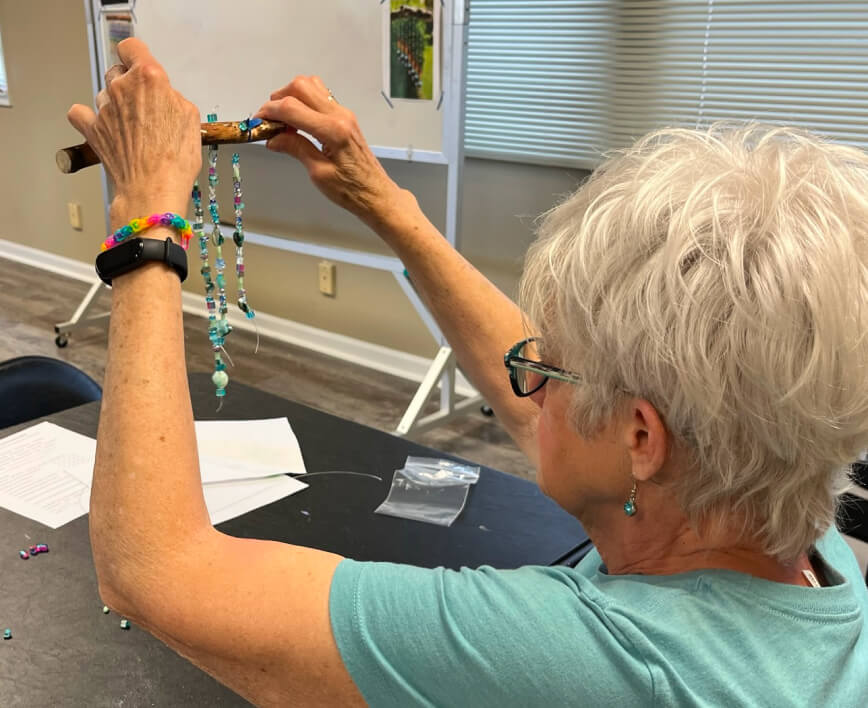 Older woman crafting with colorful beads in a classroom setting.