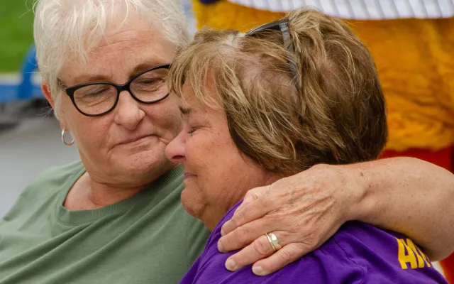 Elderly woman comforting another, both wearing casual shirts.