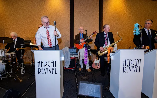 Band performing with instruments, including drums, saxophone, and guitar, in a lively setting.