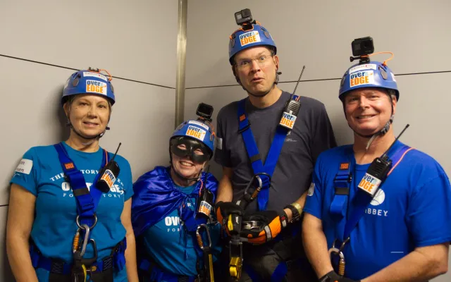 Group of four people in helmets and harnesses smiling indoors.