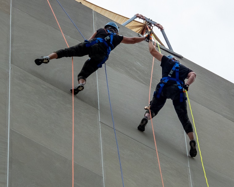 Two climbers in harnesses scaling a building.