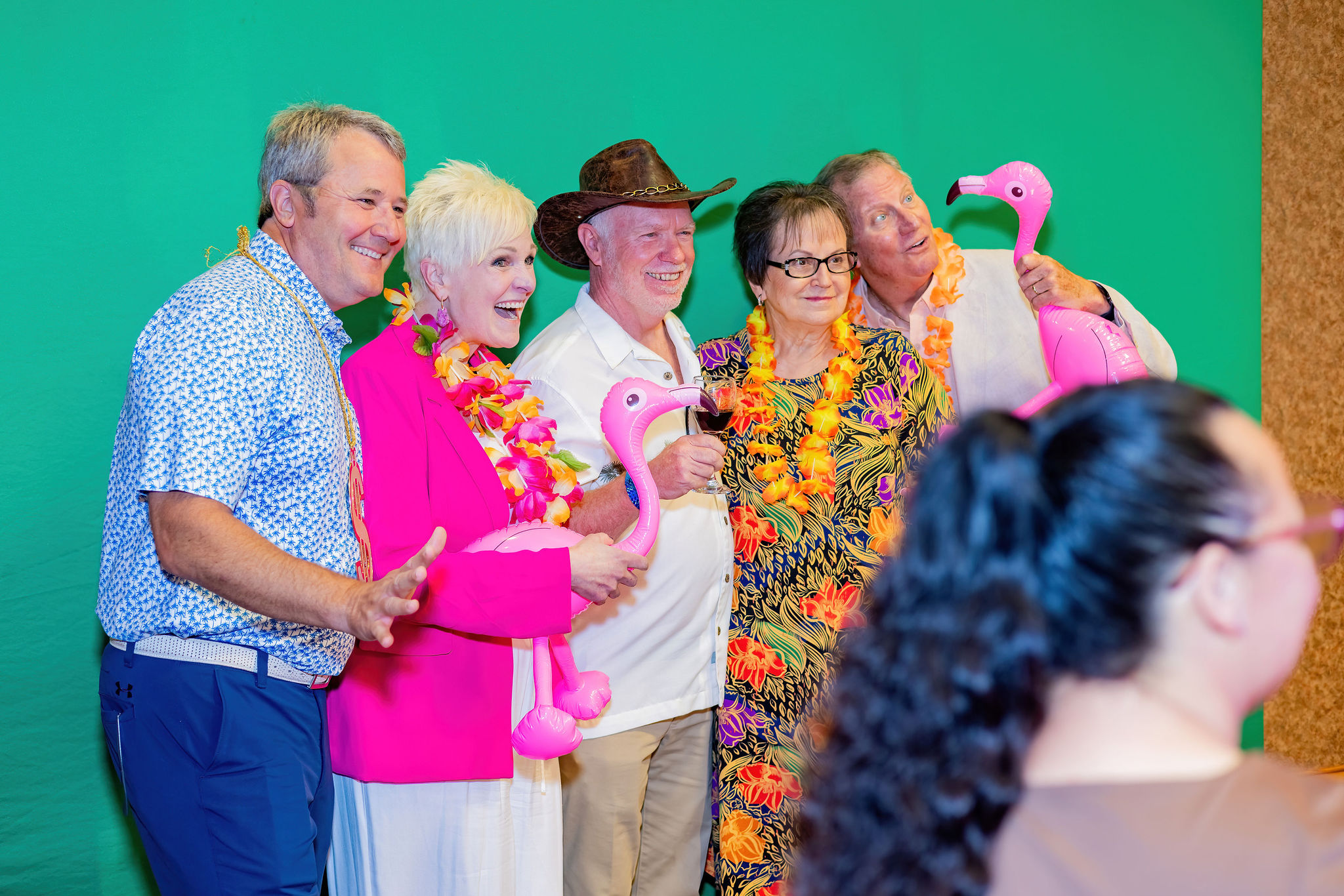 Five people in colorful attire pose with pink flamingos against a green background.