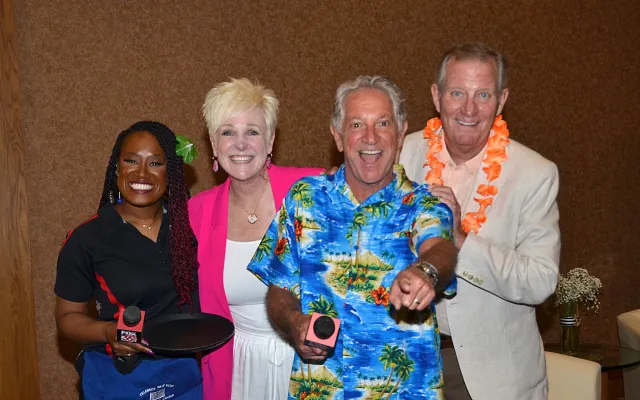 Four people smiling, two holding timers, one in a floral shirt and another with a lei.