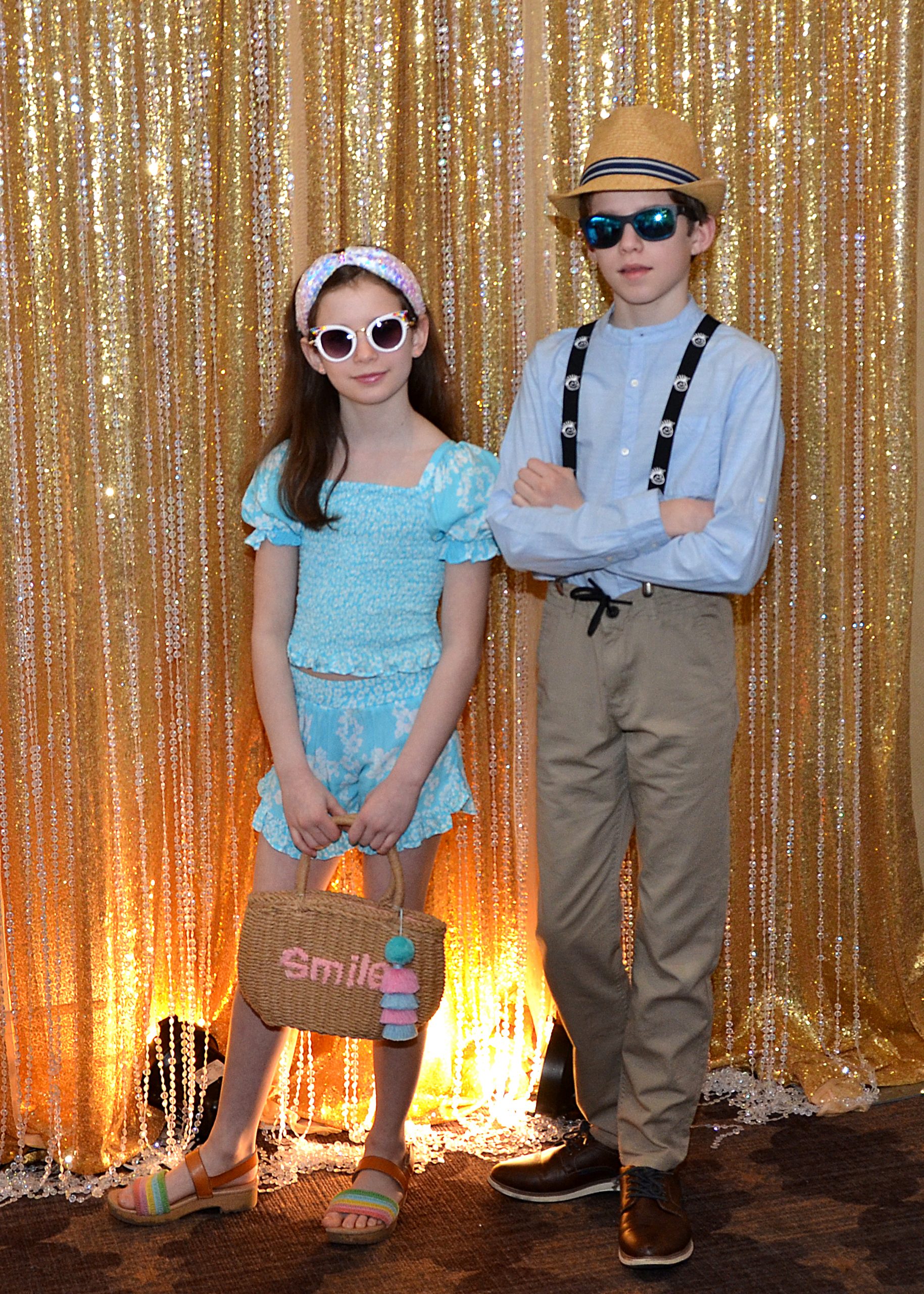 Two children in colorful outfits and sunglasses against a shimmering golden backdrop.