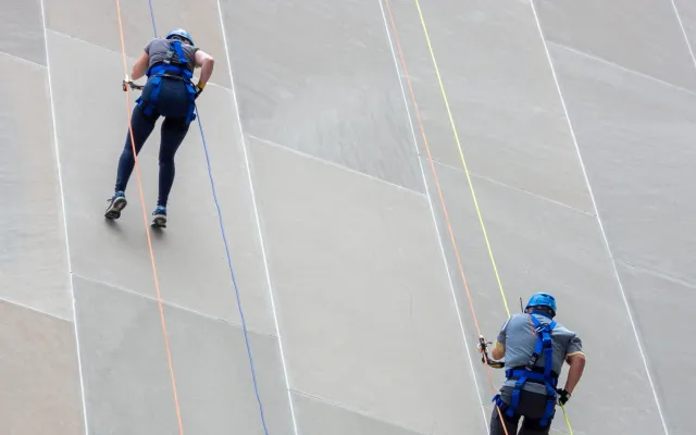 Two people rappelling down a building, wearing helmets and harnesses.