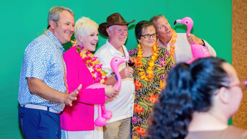 Group of five people smiling with flamingo props, colorful and festive attire.