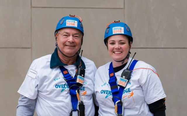Two people in helmets and harnesses smiling, wearing event shirts.