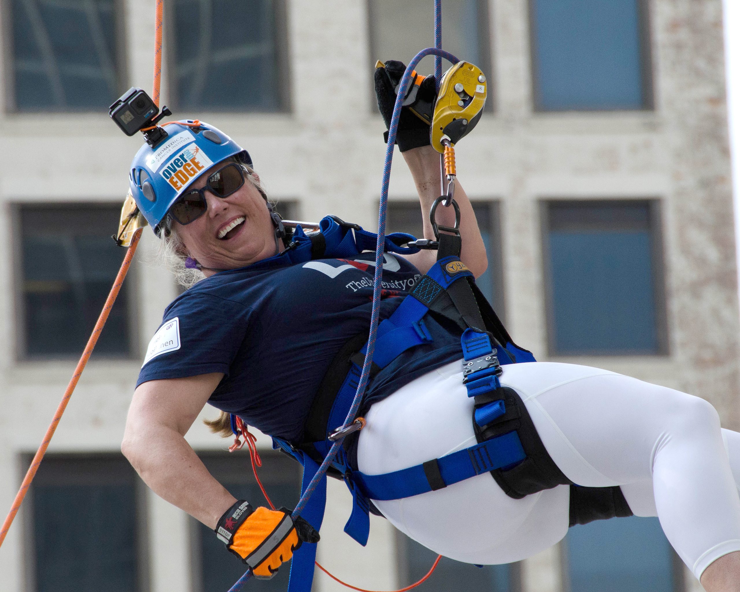 A person wearing climbing gear and helmet, happily rappelling from a building.