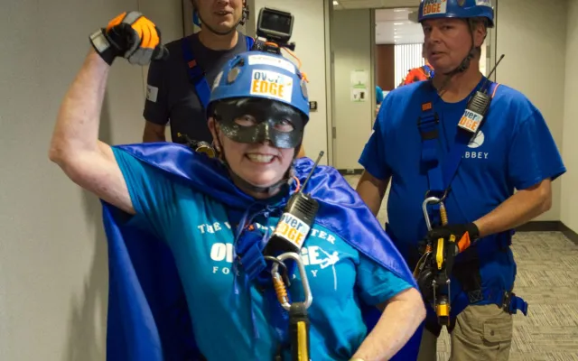 Three people in safety gear and blue attire in a hallway, one posing enthusiastically.