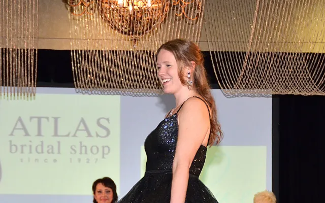 Woman in a black gown on a runway, smiling.
