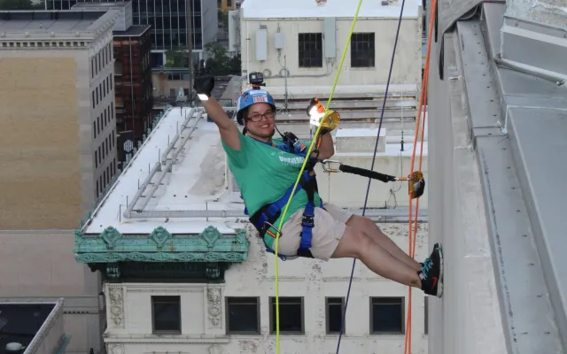 Two people rappelling down a tall city building, wearing safety gear.