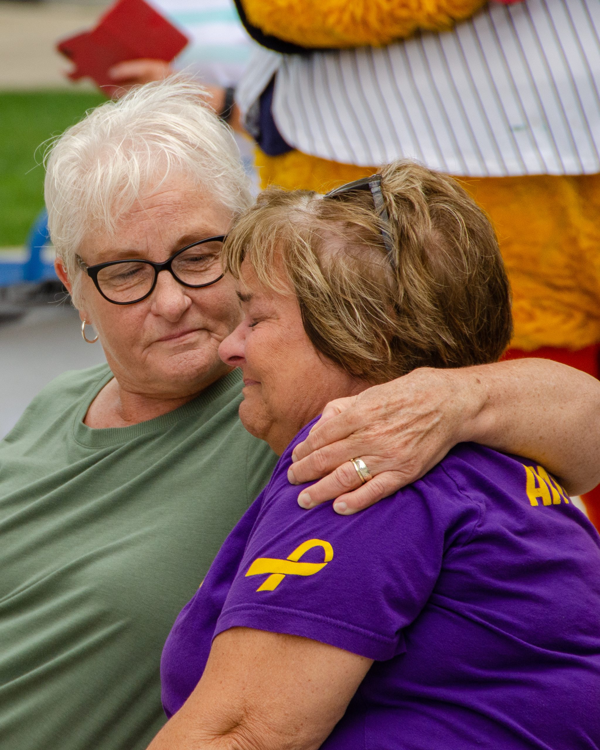 Elderly woman comforting another, both wearing casual shirts.