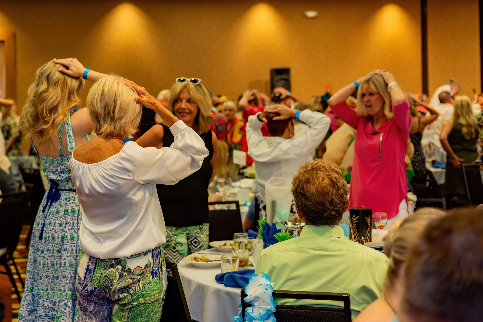 Women in a banquet hall dancing with hands on heads, colorful attire.