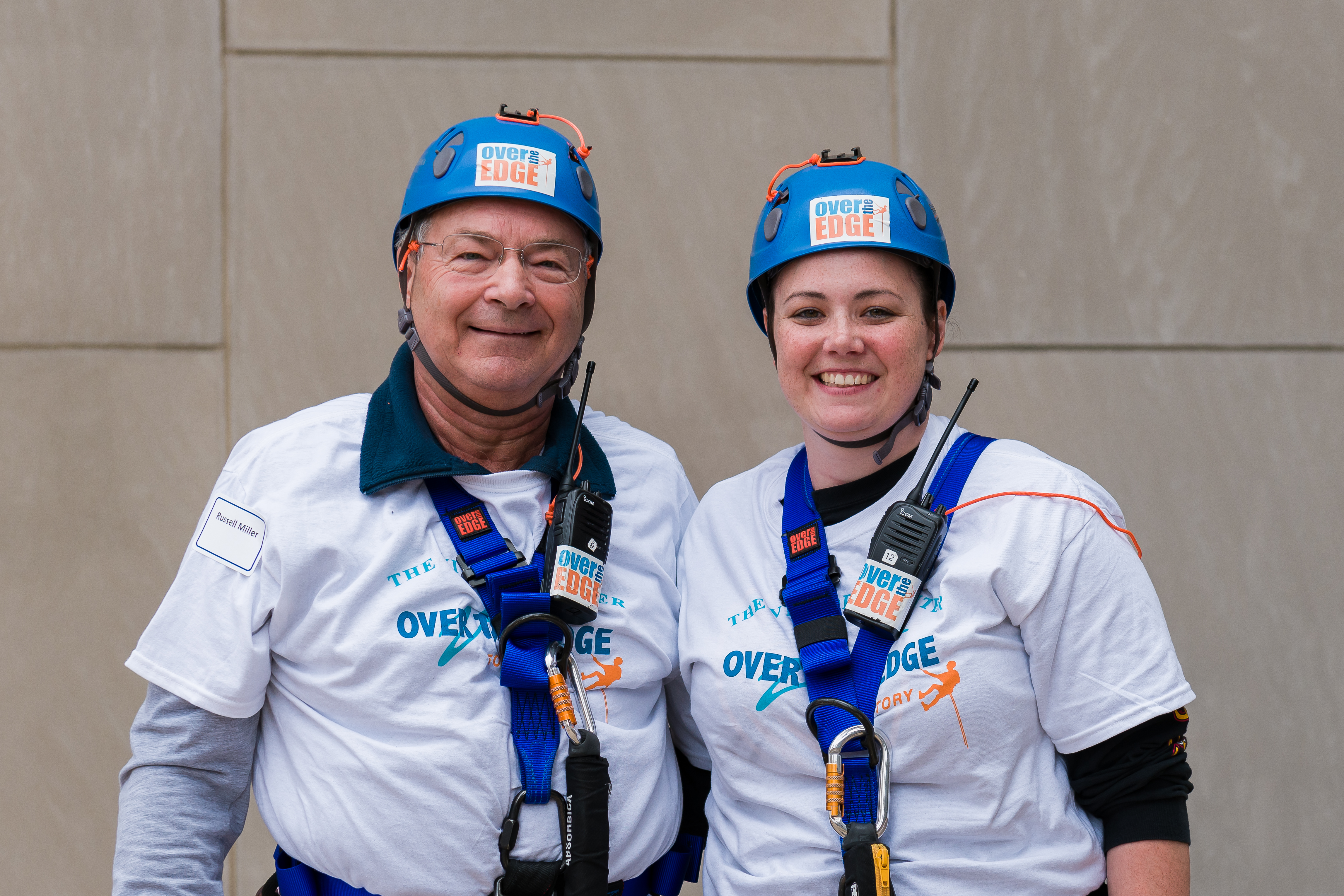 Two people in helmets and harnesses smiling, wearing event shirts.