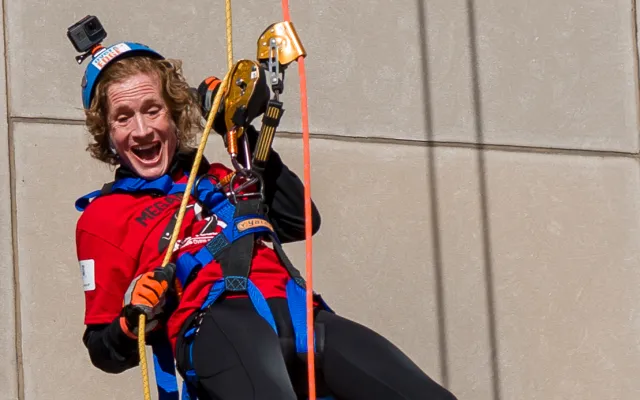 Person joyfully rappelling down a building in colorful gear.