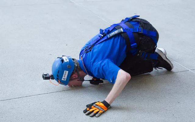 Person in blue gear kneeling on concrete, wearing a helmet and gloves.