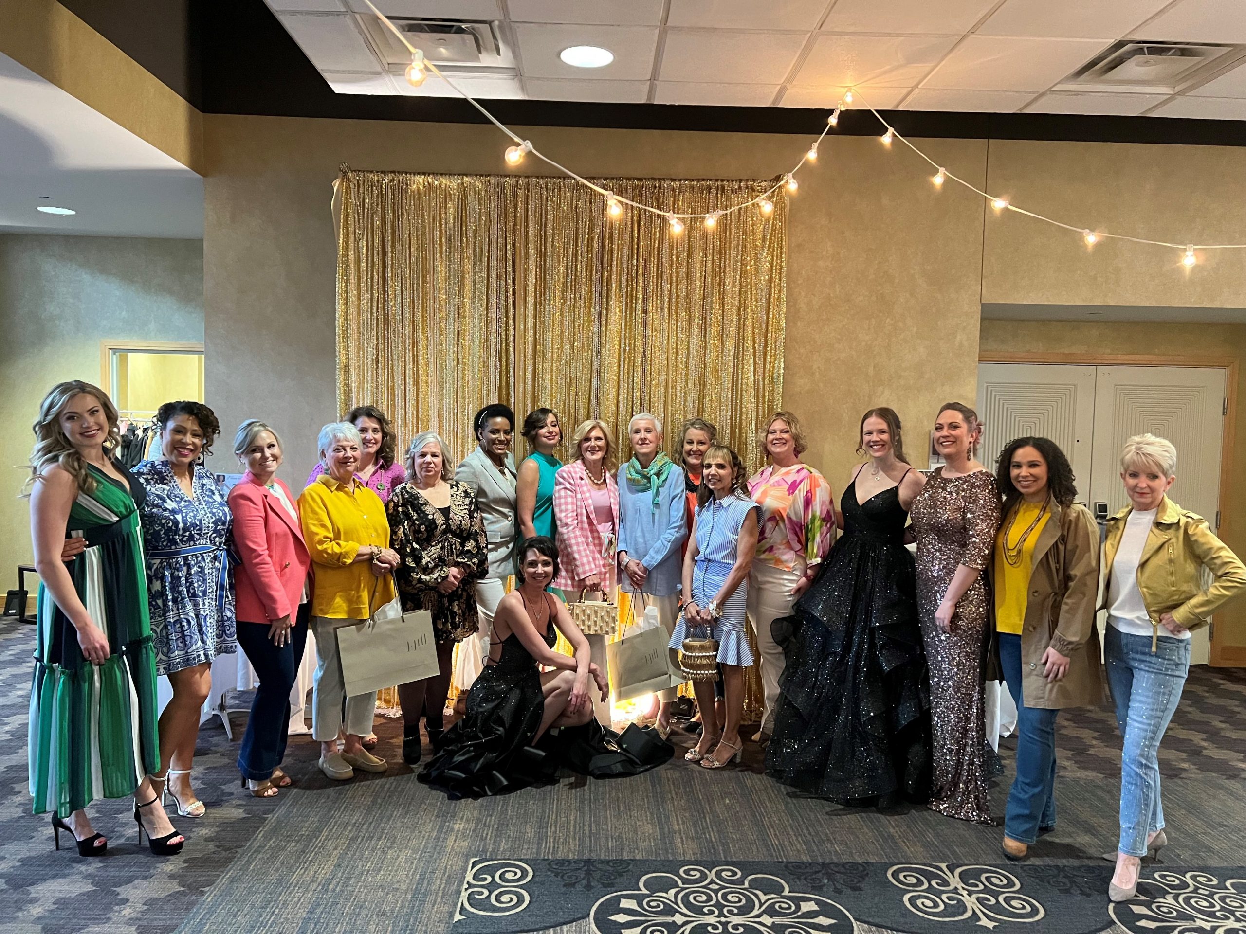 A group of women posed indoors in colorful outfits, with string lights above.