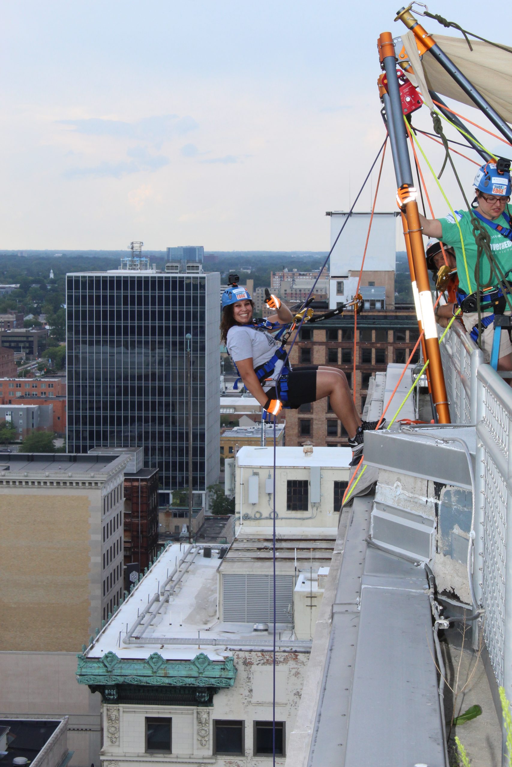 Person rappelling down a tall building in an urban setting with safety gear.